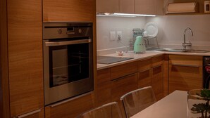 Una cocina moderna con armarios de madera, horno integrado, encimera blanca y una mesa de comedor con sillas.