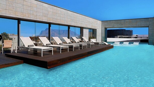 Un área de piscina exterior moderna con sillones de descanso y una terraza de madera.