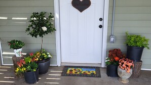 A white door with a heart-shaped welcome sign, potted plants, and a doormat with a sunflower design. - Quiet farm stay, hike, mushroom hunt, see the animals, relax, so much more! (Edmonton)