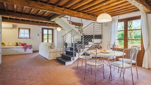 Amplia sala de estar con chimenea, una mesa de comedor con sillas, una escalera y un gran ventanal con cortinas.
