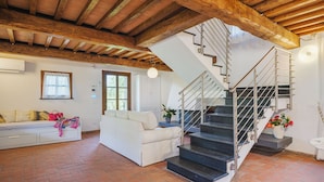 Un salón espacioso con un sofá blanco, una escalera con barandilla de metal y un techo rústico de madera.
