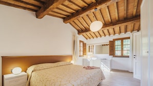 Un dormitorio con techo de madera, una cama con colcha estampada, una mesita de noche con lámpara y un aparador con espejo.