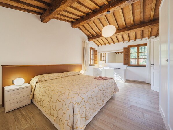 Una camera da letto con soffitto in legno, un letto con copriletto decorato, un comodino con lampada e una cassettiera con specchio.