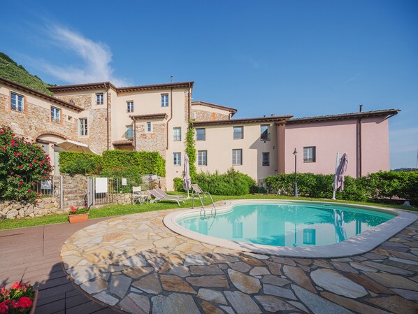 Un espace piscine avec des carreaux de pierre, un fauteuil de relaxation et un bâtiment doté de nombreuses fenêtres et de balcons.