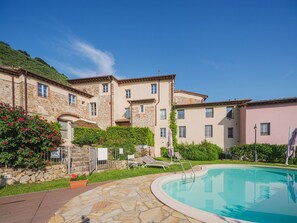 Ein Poolbereich mit einer Steinterrasse, einem Schwimmbecken und einem Gebäude mit zahlreichen Fenstern und Balkonen.