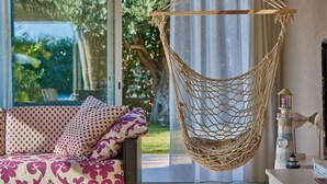 Eine Hängestuhlkorbschaukel, ein gemustertes Sofa mit Kissen und ein Blick ins Grüne durch ein Fenster.