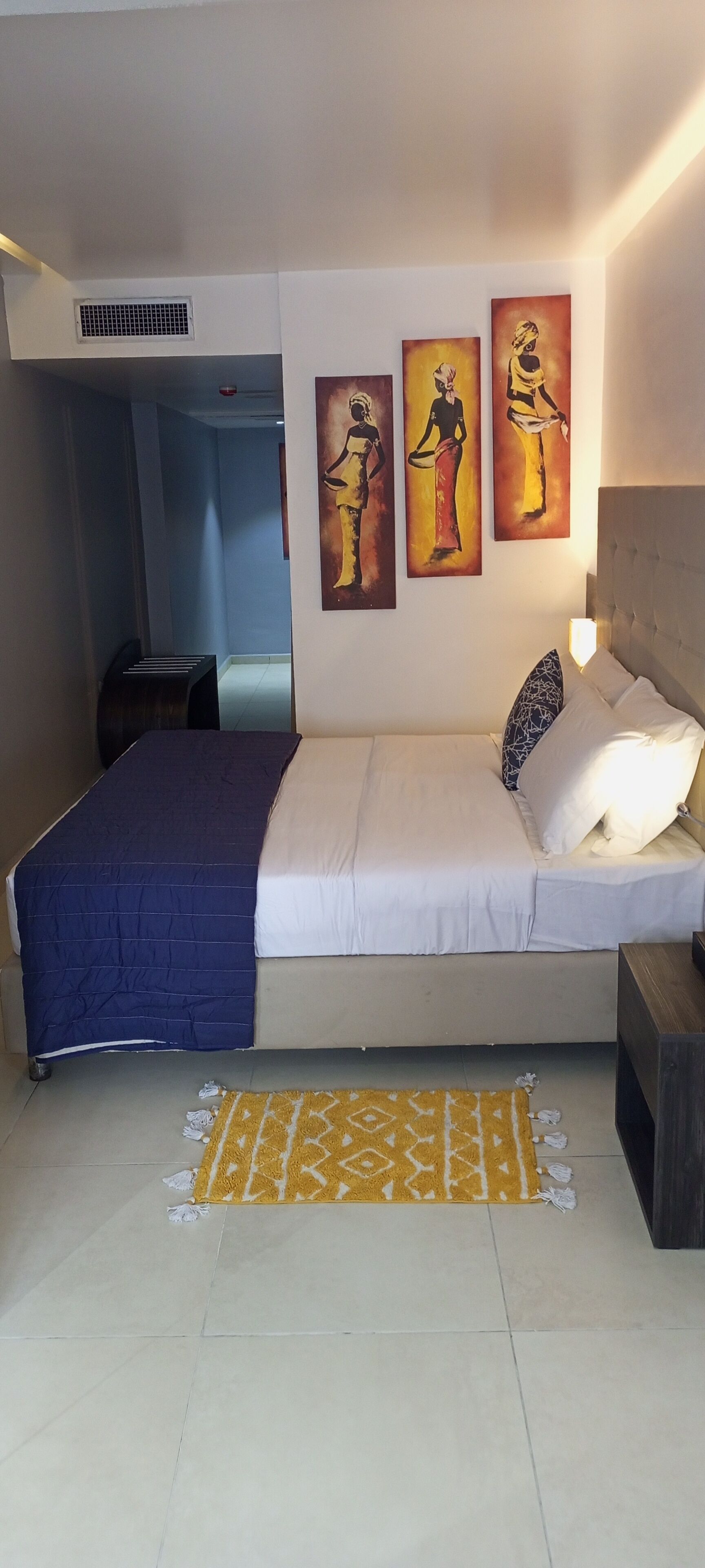 A bedroom with a bed, a nightstand, a bedside lamp, and three wall-mounted paintings.