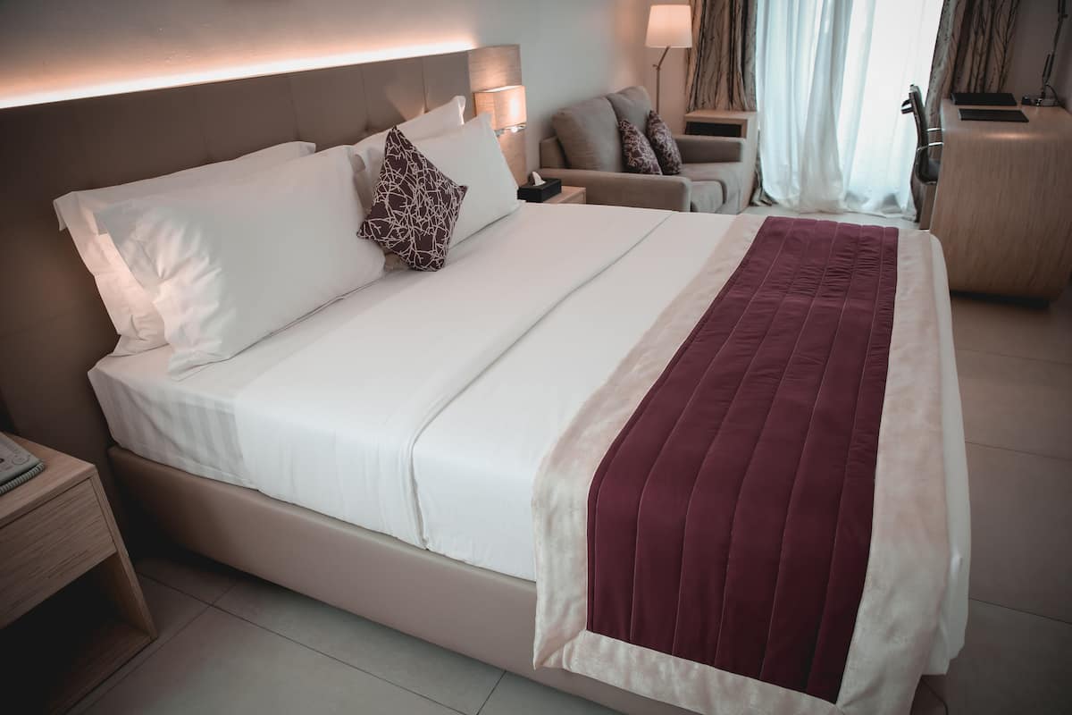 A hotel room with a large bed, a bedside table with a lamp, a chair, and a desk.