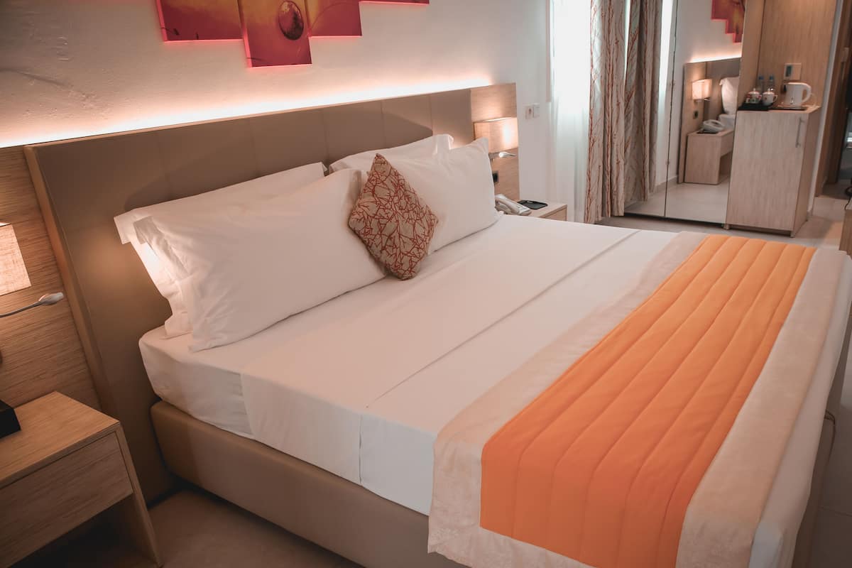 A hotel room with a bed, bedside tables, a nightstand, a lamp, a mirror, and a wardrobe.