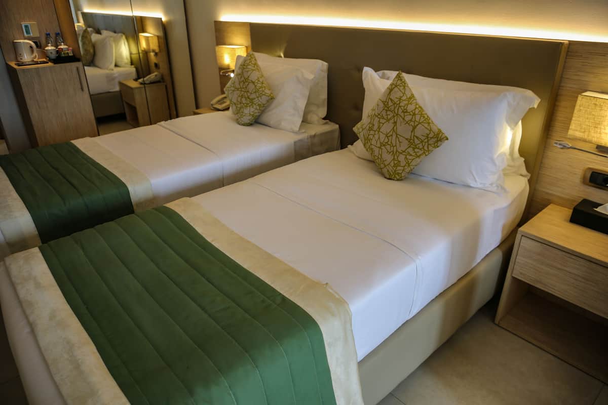 Two single beds with green and white bedding, bedside tables with lamps, and a wooden headboard.