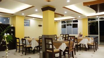 A dining area with multiple tables and chairs, wooden pillars, and a tiled floor.