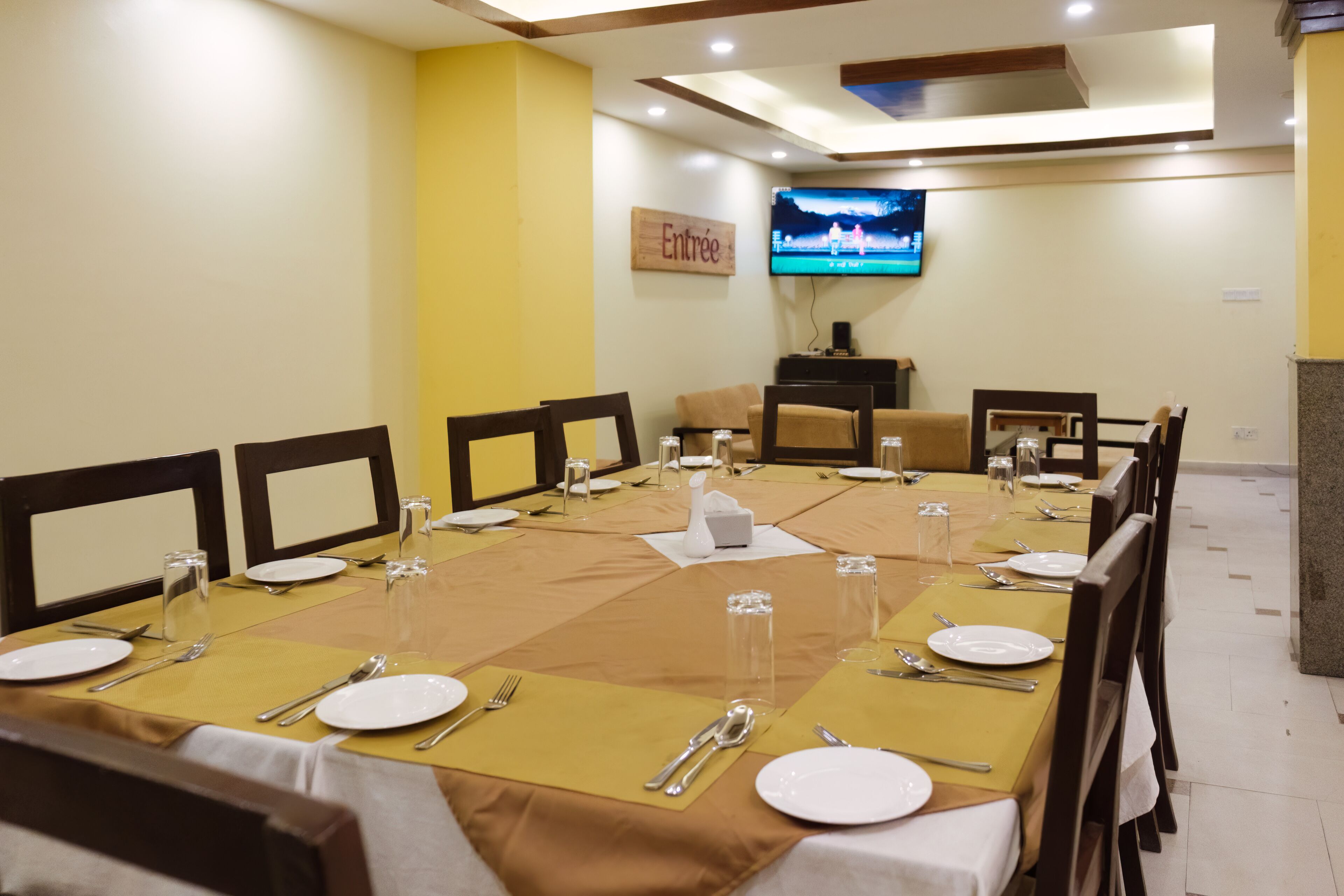 Un salón de conferencias con una larga mesa dispuesta para una reunión, equipado con sillas, platos, cubiertos y vasos.