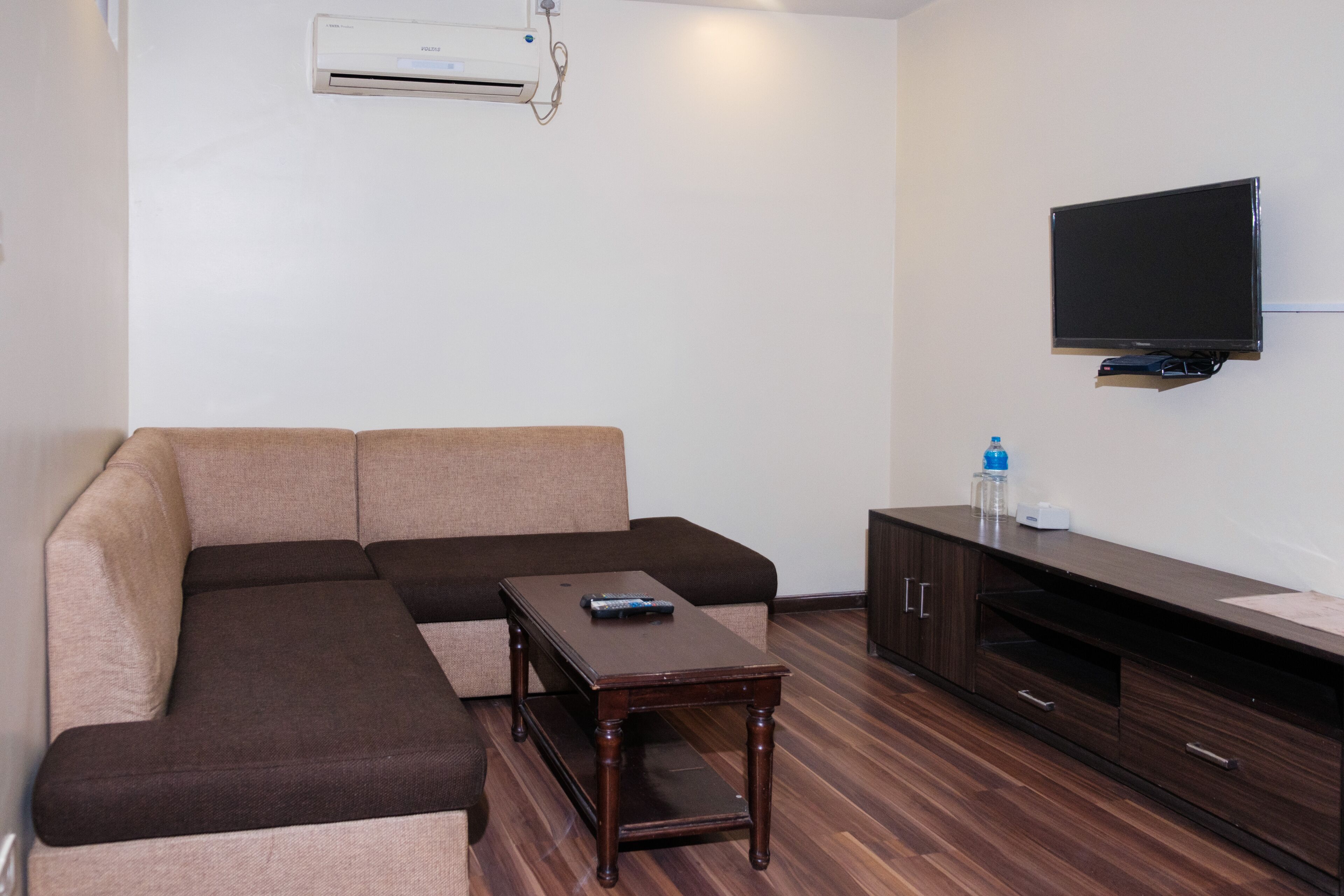 A living room with a sectional sofa, a wooden coffee table, a flat-screen TV, and a dark wooden entertainment unit.