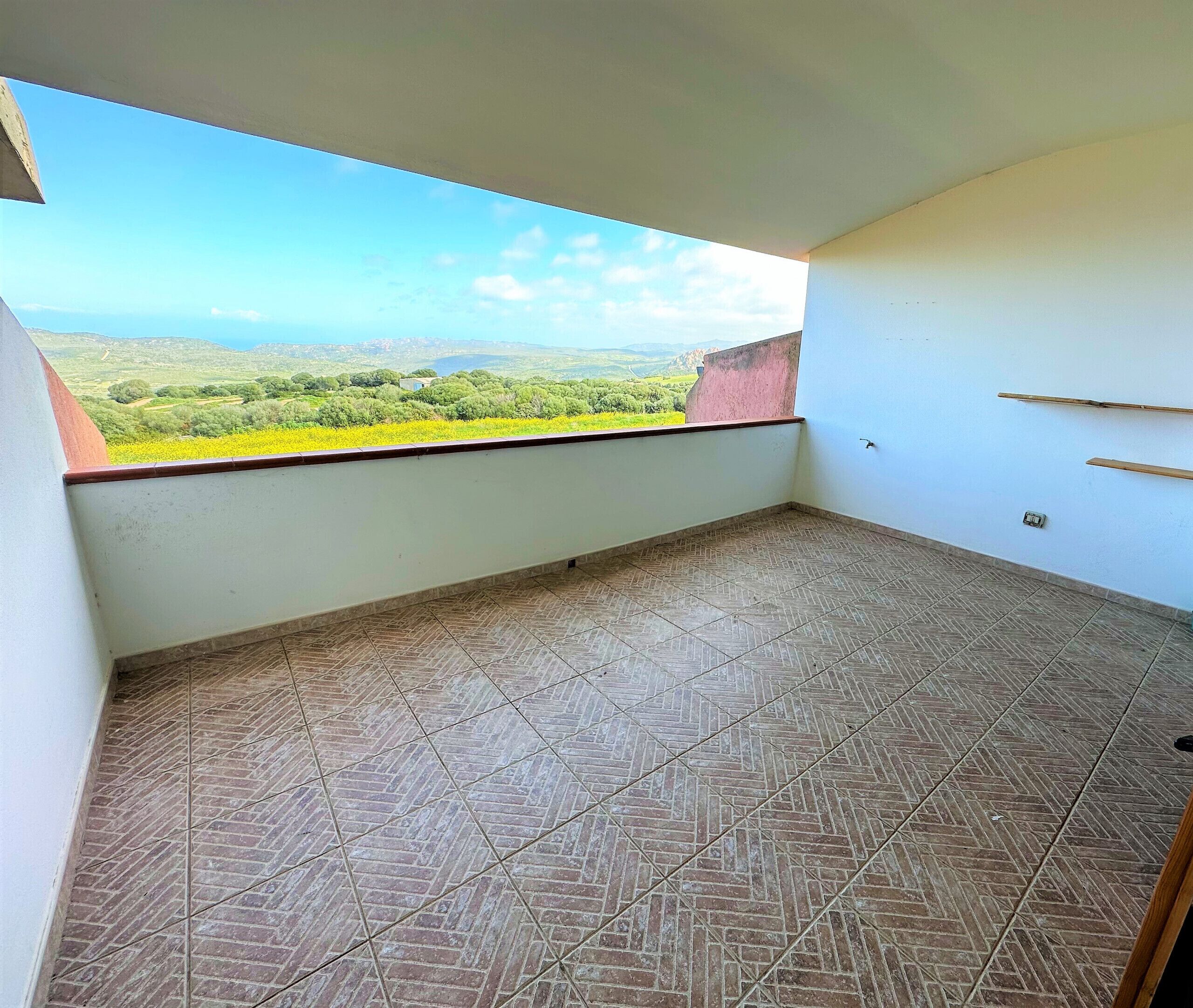 A balcony with a tiled floor and a view of a green landscape.