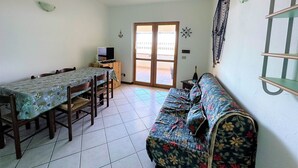 Una stanza piccola e ben illuminata con un tavolo da pranzo, sedie, un divano, una TV e una porta che dà sull'esterno.