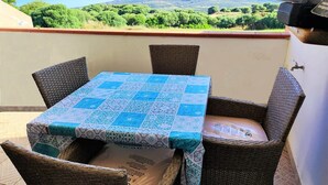 Un balcone con sedie in vimini e un tavolo ricoperto da una tovaglia a motivi blu e bianchi.