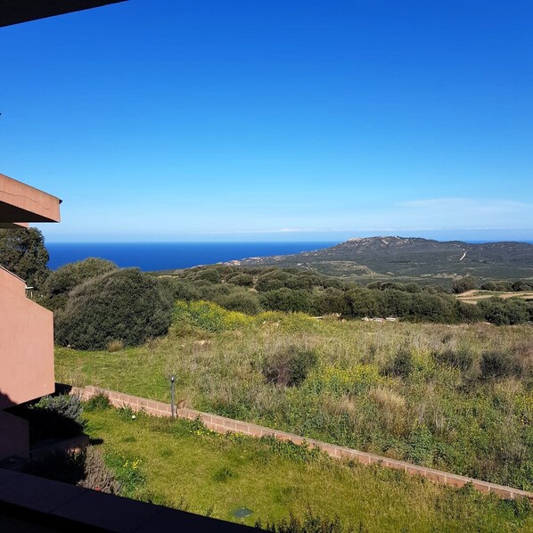 A balcony with a view of a coastal landscape, including a road and distant hills.
