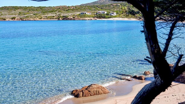 Paesaggio costiero con acqua cristallina, spiaggia sabbiosa e case su una collina.