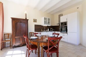 A dining area with a wooden table and chairs, a wooden door, and a kitchen with white cabinets and appliances.