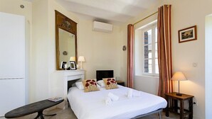 Una camera da letto con un letto, una panca, un camino, uno specchio, una finestra con tende e un comodino con una lampada.