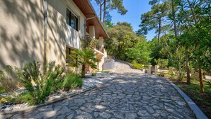 Un chemin de pierre mène à un bâtiment dont la façade est recouverte d’enduit et qui possède un balcon en bois.