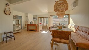 Un vaste espace de vie comprenant une table à manger en bois, un canapé et un luminaire suspendu en rotin.