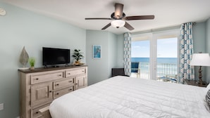 Quarto com cama grande, ventilador de teto, televisão, cômoda e vista para o mar.