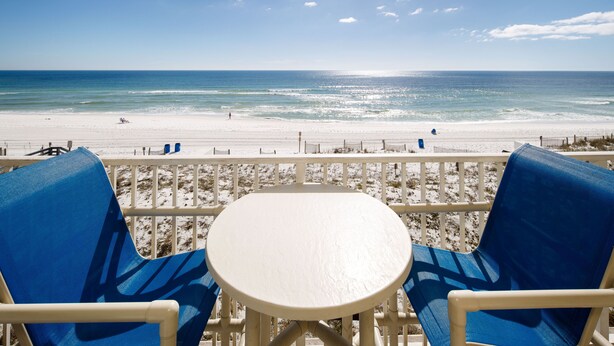 Vista da praia a partir de uma varanda, com uma mesa e duas cadeiras azuis.