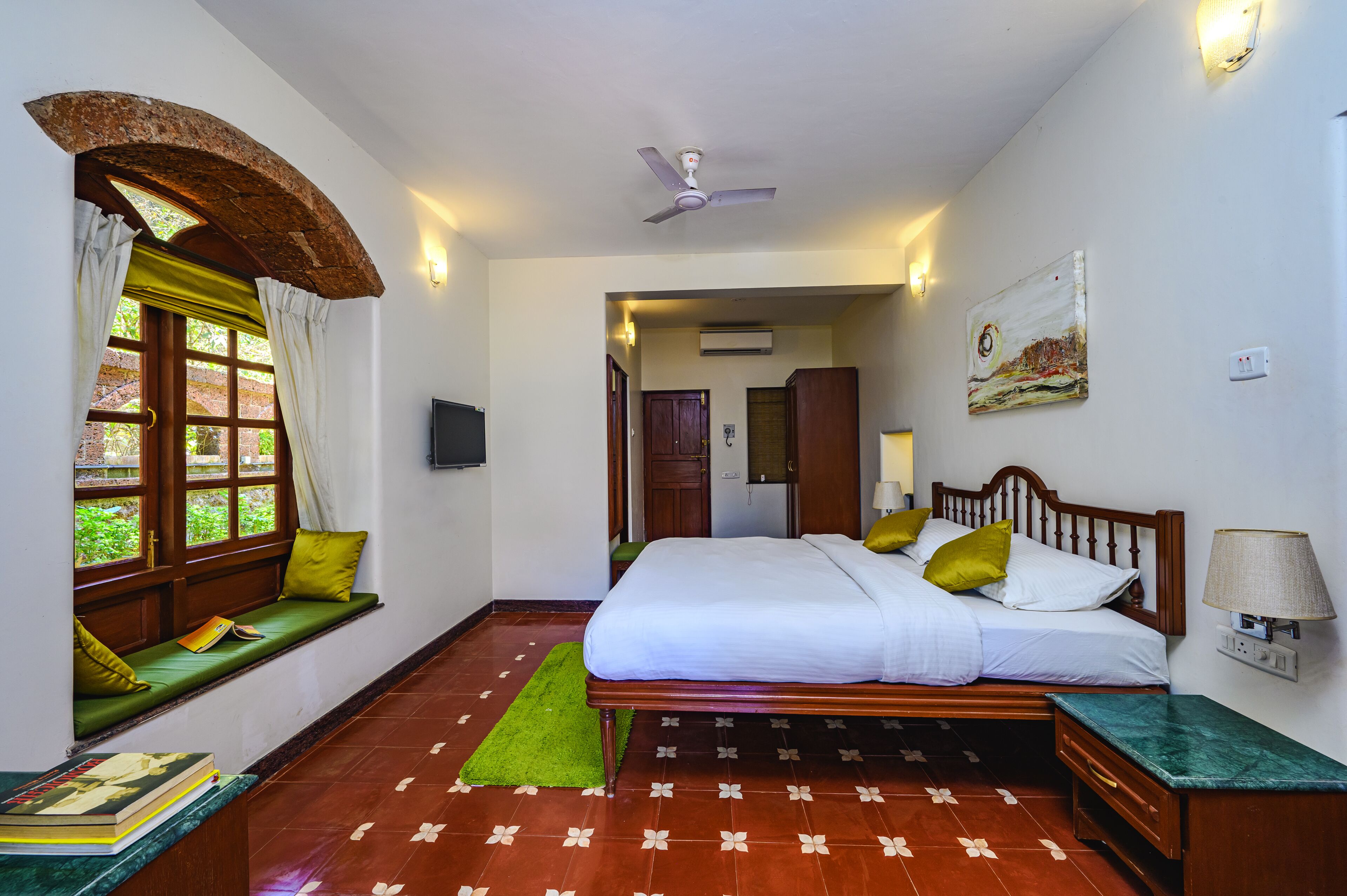 A bedroom with a bed, a window seat, a ceiling fan, and a wall-mounted lamp.