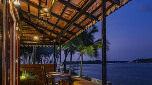 Un área de comedor al aire libre con vista al mar, mobiliario de madera y techo de paja.