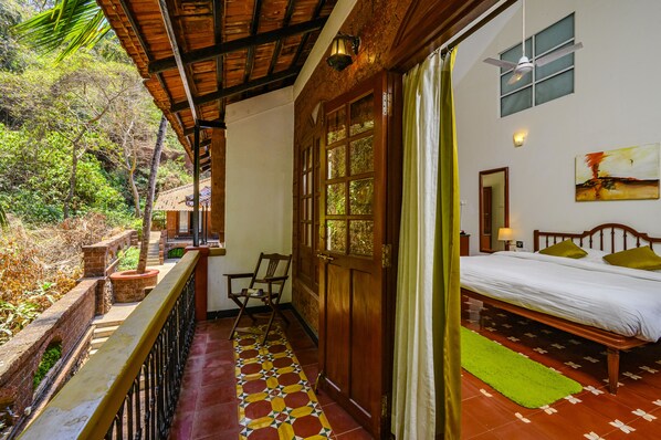 A room with a bed, a window, a painting, and a balcony with a railing.