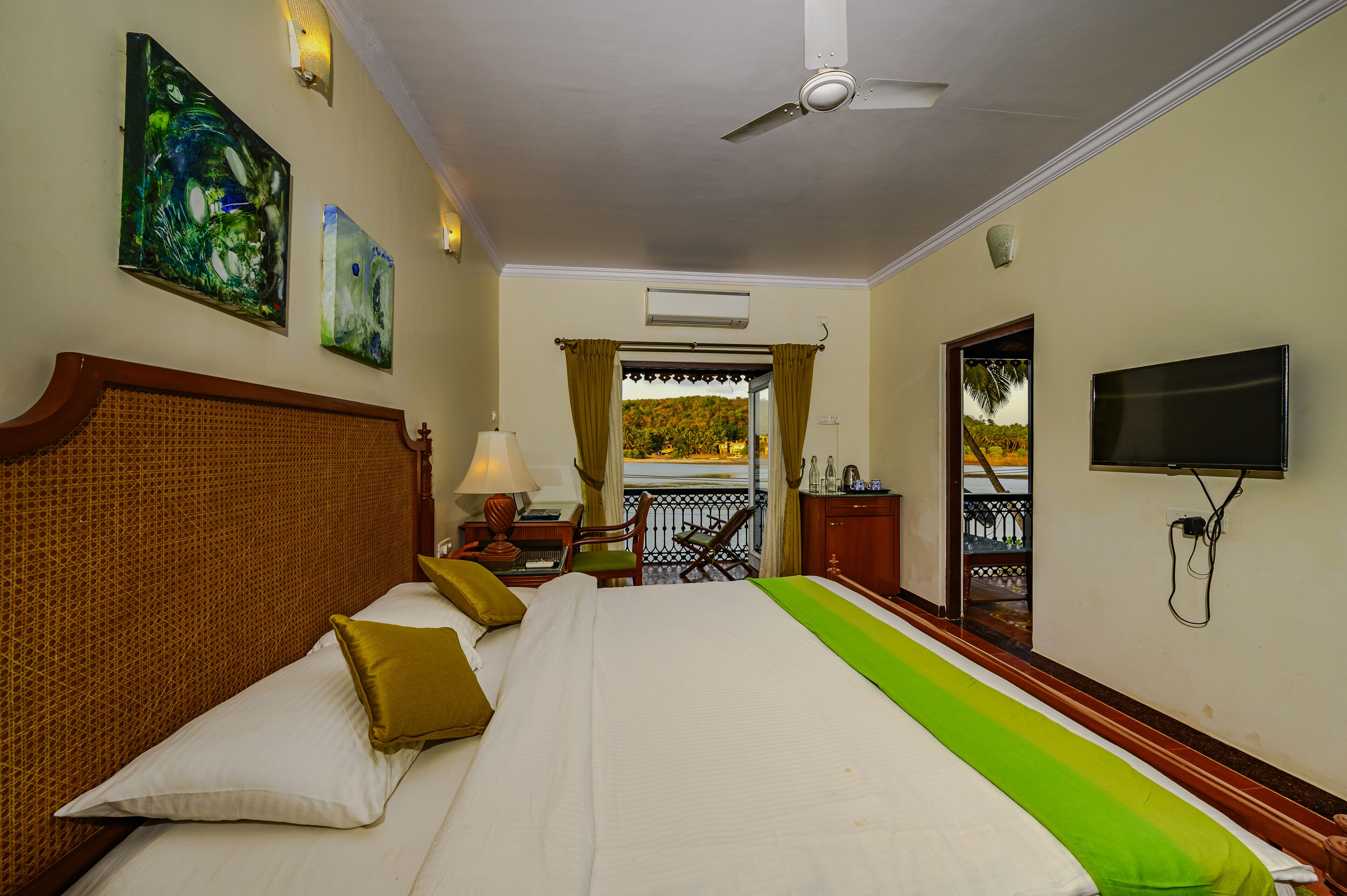 A hotel room with a large bed, a television, artwork on the walls, and a balcony with a view.
