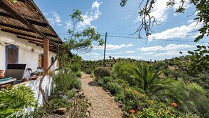 A rustic house with a gravel path leading to a wooden door, surrounded by lush greenery and a clear sky. - Rustic 3-bedroom Country Retreat With Pool, Free Wi-fi, and Breathtaking Views (Tavira)