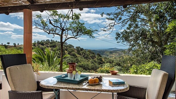 A terrace with wicker chairs, a table with a tray of lemons, a bowl, and a book, overlooking a lush landscape. - Rustic 3-bedroom Country Retreat With Pool, Free Wi-fi, and Breathtaking Views (Tavira)