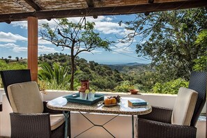 Una terrazza con sedie in vimini, un tavolo con un vassoio di limoni, una ciotola e un libro, con vista su un paesaggio lussureggiante.
