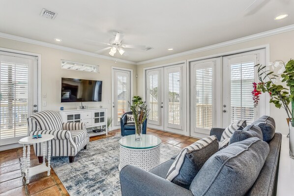 A spacious living room with a large TV, comfortable seating, and a ceiling fan.