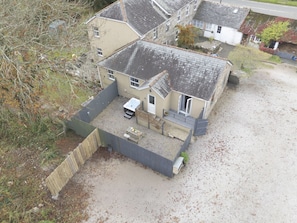 Two-story house with a sloped roof and detached garage, set amidst a fenced backyard with patio area.