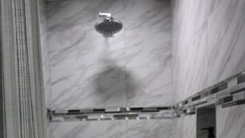 Un baño con paredes de mármol, ducha y un pequeño estante con una botella.