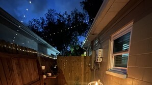 Une terrasse avec un sol à motifs géométriques, une clôture en bois, une petite table avec des chaises et des guirlandes lumineuses.