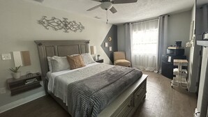 Une chambre avec un grand lit, un ventilateur de plafond, un bureau et un réfrigérateur.
