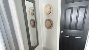 Un couloir avec une porte noire, un miroir et trois chapeaux accrochés au mur.