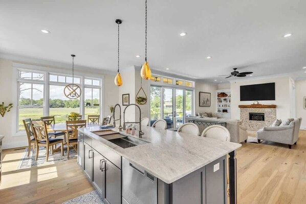 A modern kitchen with a large island, pendant lights, and a dining area with chairs.