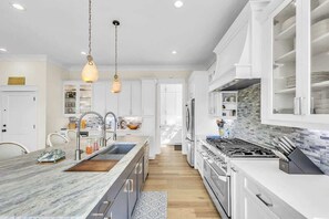 A modern kitchen with white cabinetry, a marble countertop, a gas stove, and hanging pendant lights.
