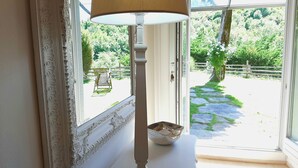 Une pièce avec un grand miroir blanc à motifs, une table blanche sur laquelle se trouve un bol, et une vue sur un jardin par une porte vitrée.