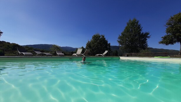 Une piscine aux eaux cristallines, dotée de chaises longues et offrant une vue sur les montagnes en arrière-plan.