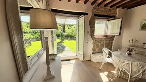 Une pièce avec un mur en pierre, une table blanche recouverte d’une nappe en dentelle et une lampe.
