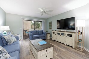 A living room with a blue sofa, a coffee table, a TV, and a cabinet. - 167 Colonnade: Fully updated Villa, Pool and Hot Tub, Gas Grills, Free Bikes (Hilton Head Island)