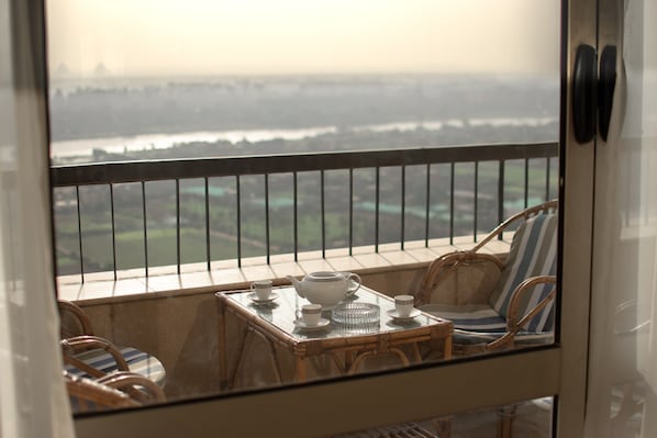 A balcony with wicker furniture, a table with a teapot, cups, and a decorative bowl.