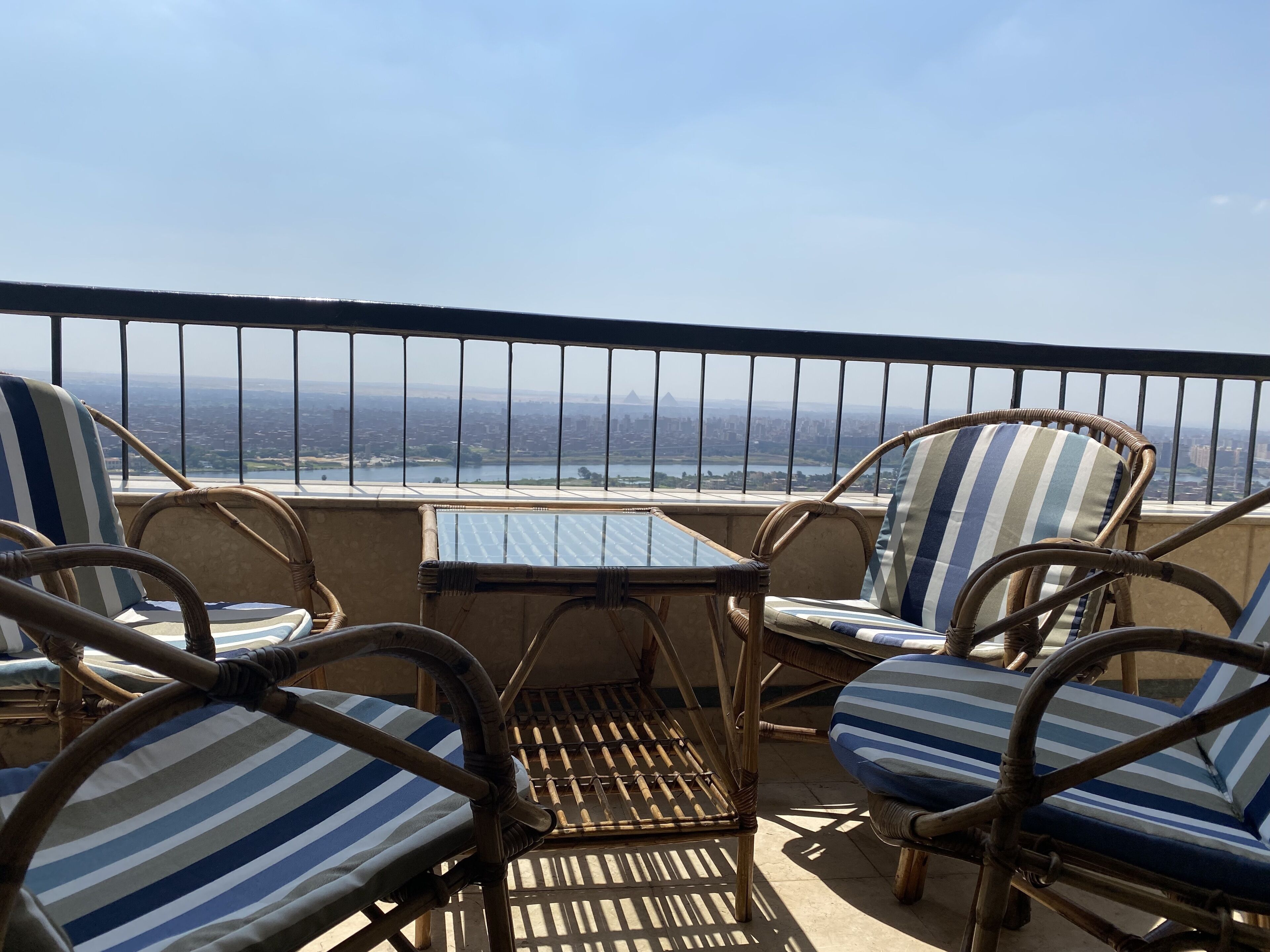 A balcony with wicker chairs and a table, overlooking a cityscape.