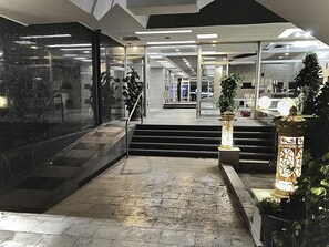A modern lobby with marble flooring, a staircase, and a glass entrance leading to a well-lit interior.